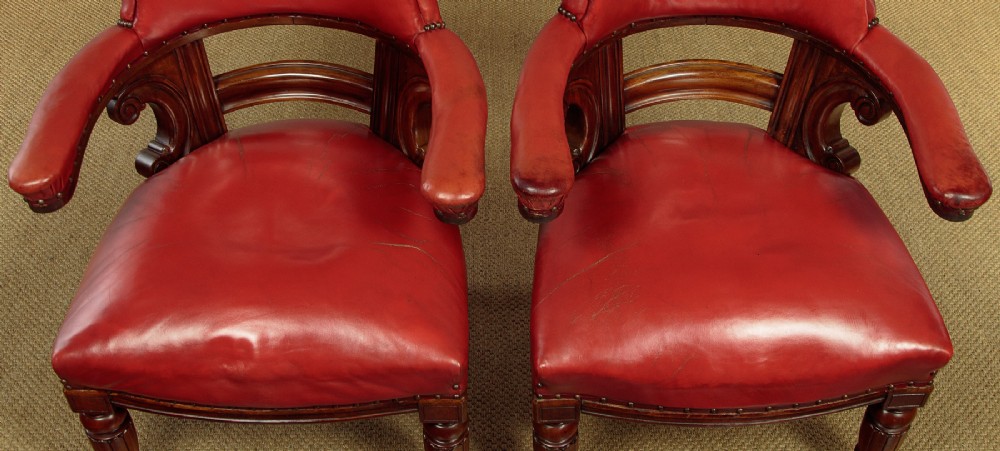 A pair of late Victorian walnut tub armchairs with red leather upholstery, studded brass trim, turned front legs, and carved scroll arm supports. View IV