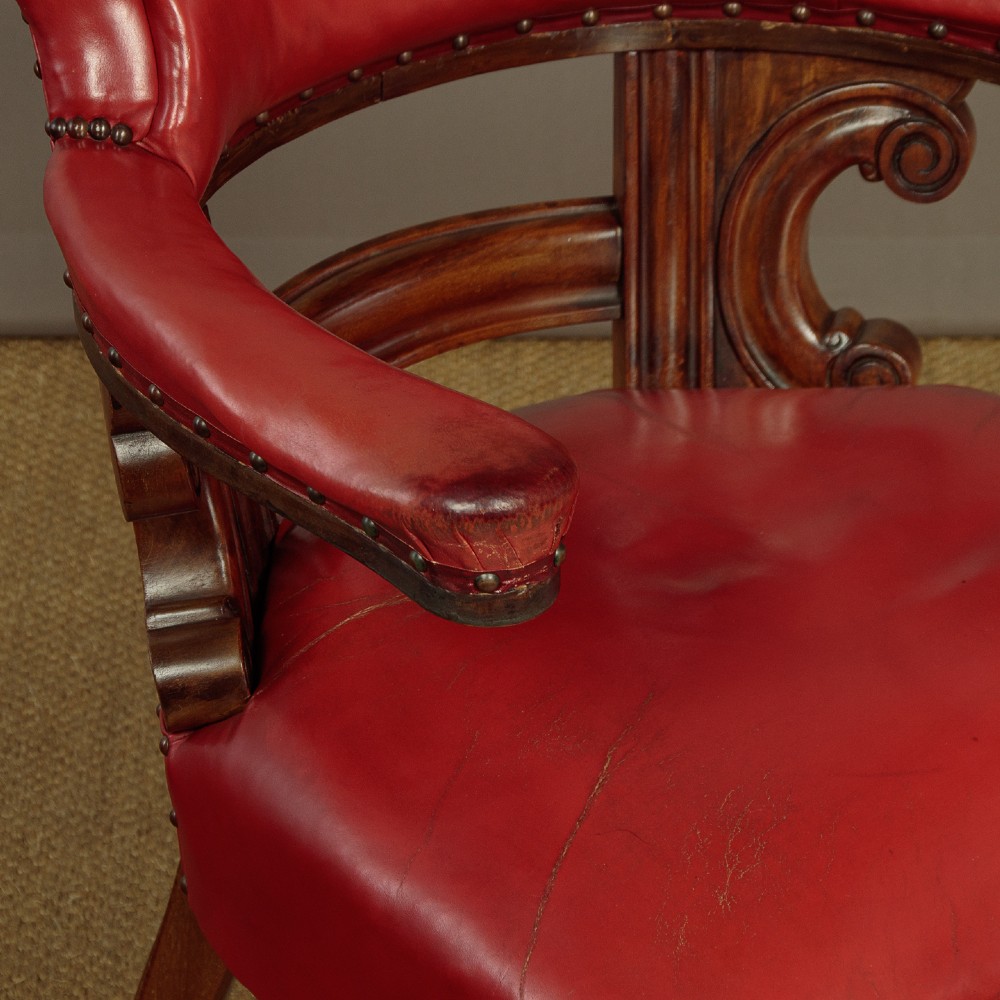 A pair of late Victorian walnut tub armchairs with red leather upholstery, studded brass trim, turned front legs, and carved scroll arm supports. View V