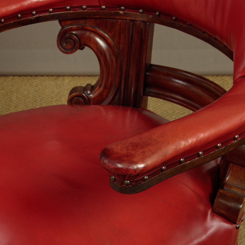 A pair of late Victorian walnut tub armchairs with red leather upholstery, studded brass trim, turned front legs, and carved scroll arm supports. View VI