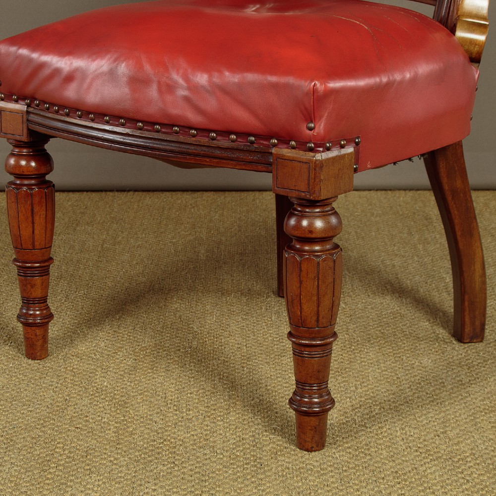 A pair of late Victorian walnut tub armchairs with red leather upholstery, studded brass trim, turned front legs, and carved scroll arm supports. View X