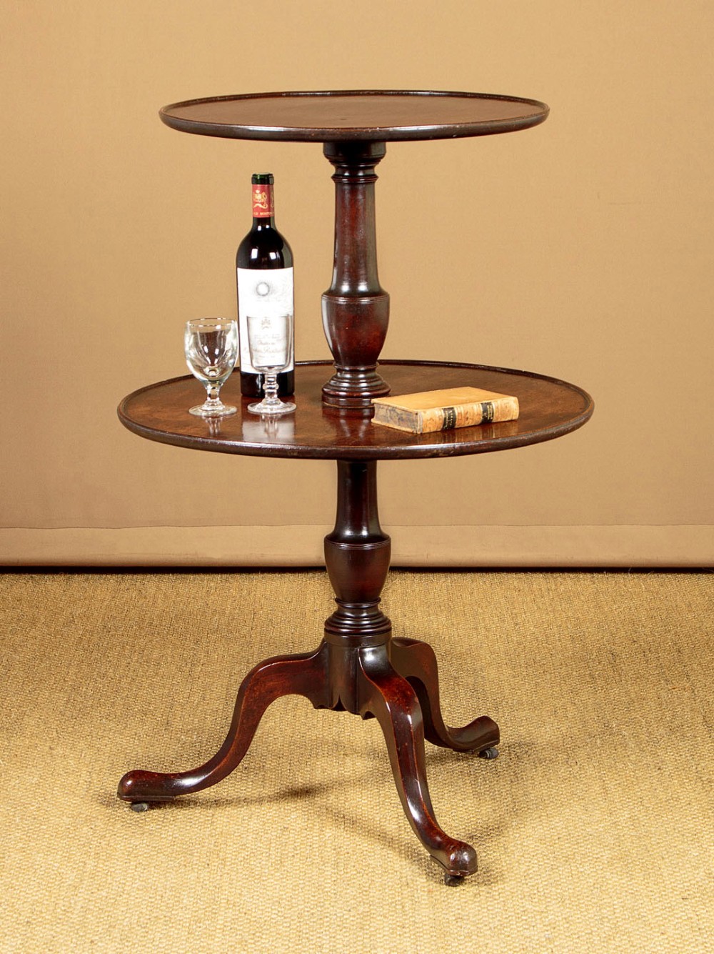 A two-tiered Georgian mahogany dumb waiter with turned baluster columns and a tripod base on brass castors. View II