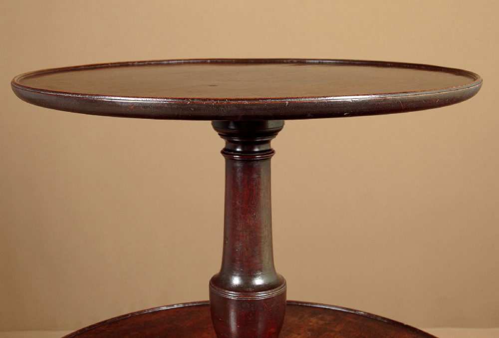A two-tiered Georgian mahogany dumb waiter with turned baluster columns and a tripod base on brass castors. View V