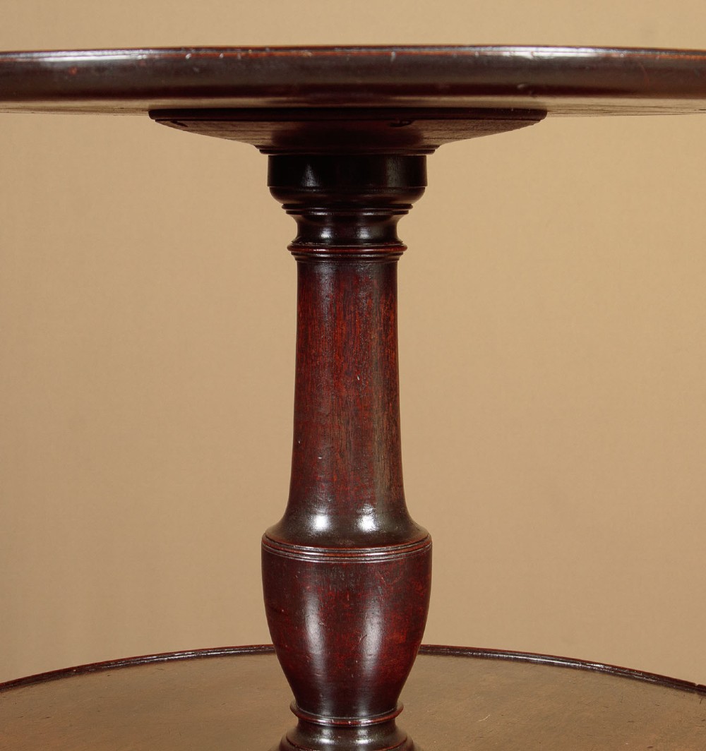 A two-tiered Georgian mahogany dumb waiter with turned baluster columns and a tripod base on brass castors. View VII