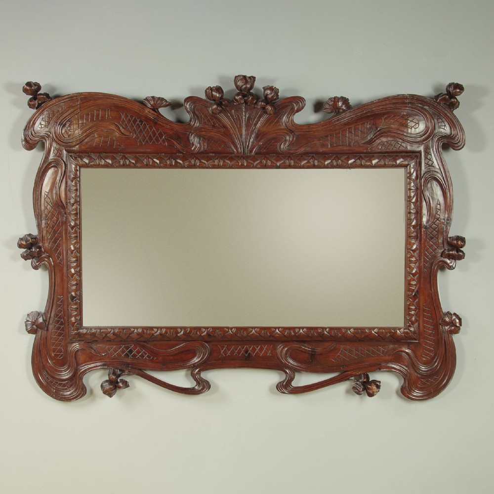 An antique Art Nouveau wall mirror featuring an intricately carved dark wood frame with sweeping whiplash curves and floral accents surrounding rectangular mirror glass.