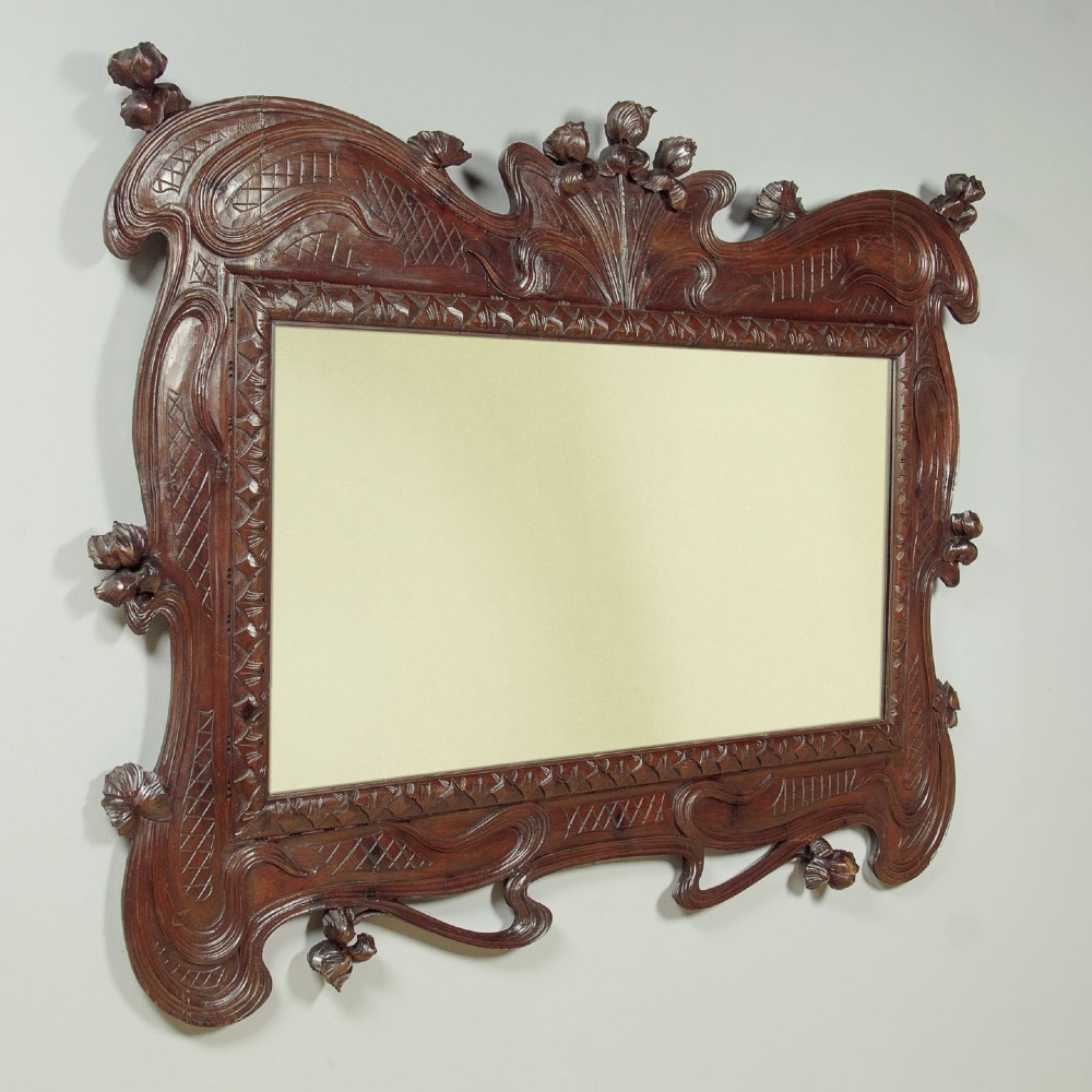 An antique Art Nouveau wall mirror featuring an intricately carved dark wood frame with sweeping whiplash curves and floral accents surrounding rectangular mirror glass. View II