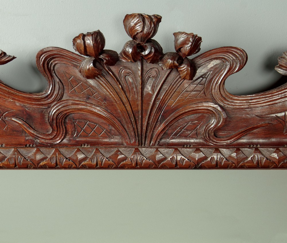 An antique Art Nouveau wall mirror featuring an intricately carved dark wood frame with sweeping whiplash curves and floral accents surrounding rectangular mirror glass. View III