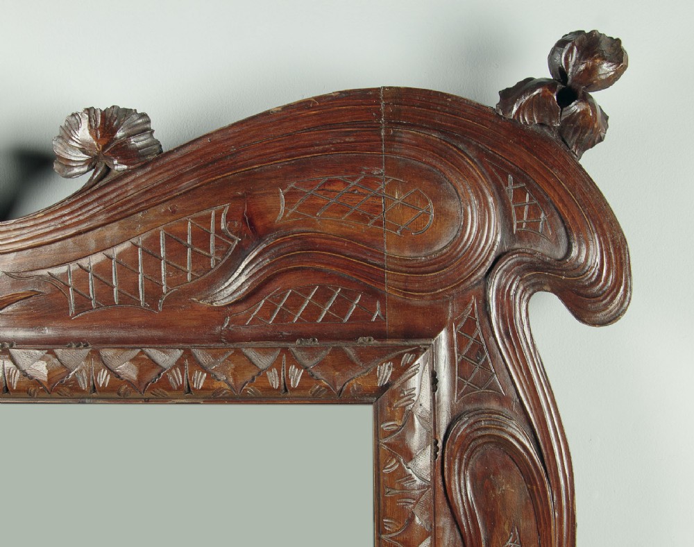 An antique Art Nouveau wall mirror featuring an intricately carved dark wood frame with sweeping whiplash curves and floral accents surrounding rectangular mirror glass. View IV