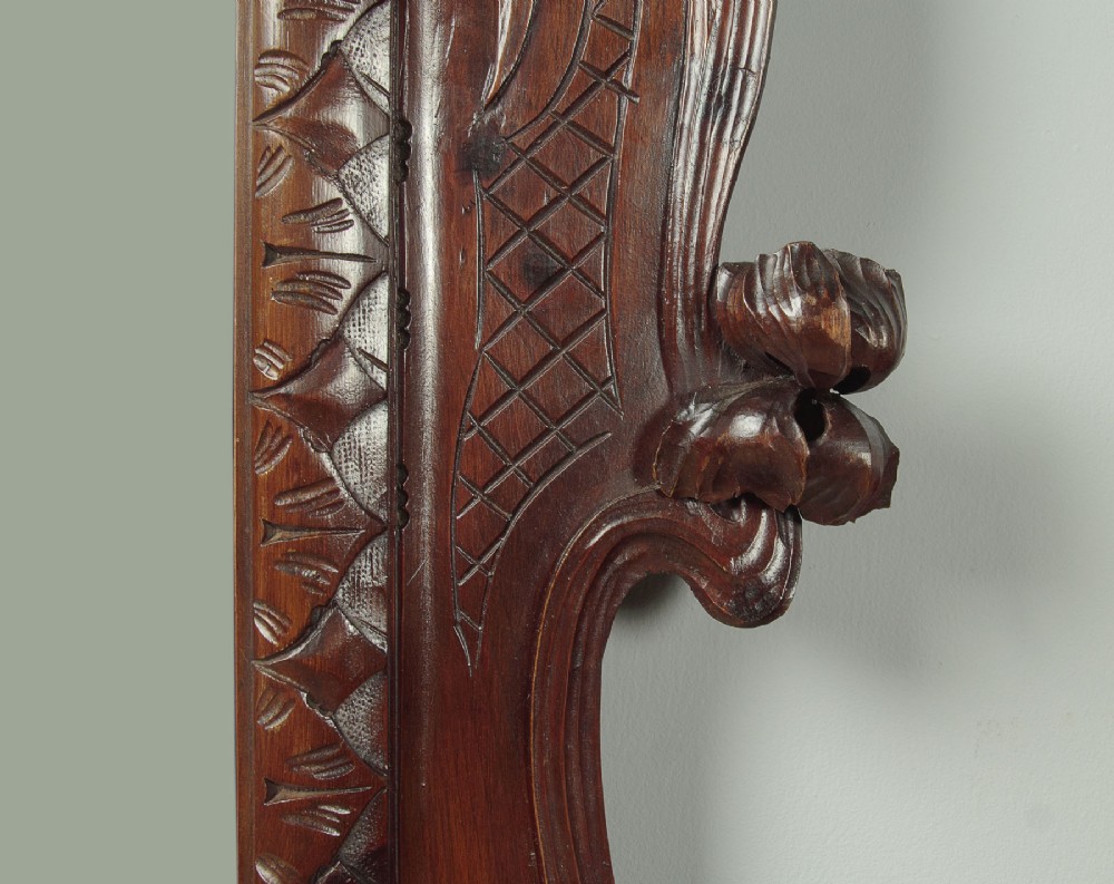 An antique Art Nouveau wall mirror featuring an intricately carved dark wood frame with sweeping whiplash curves and floral accents surrounding rectangular mirror glass. View VIII