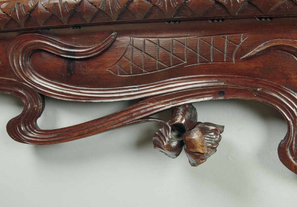 An antique Art Nouveau wall mirror featuring an intricately carved dark wood frame with sweeping whiplash curves and floral accents surrounding rectangular mirror glass. View IX