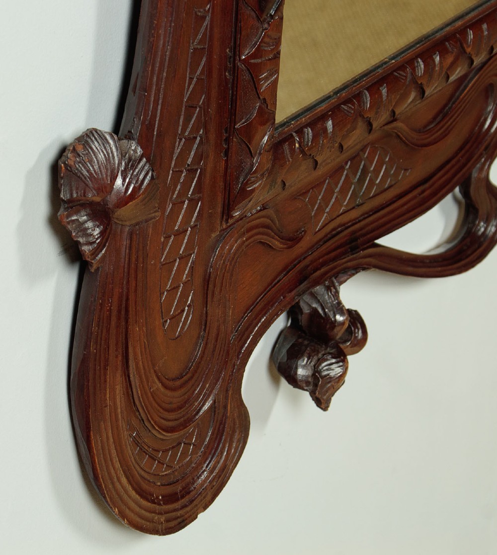 An antique Art Nouveau wall mirror featuring an intricately carved dark wood frame with sweeping whiplash curves and floral accents surrounding rectangular mirror glass. View X