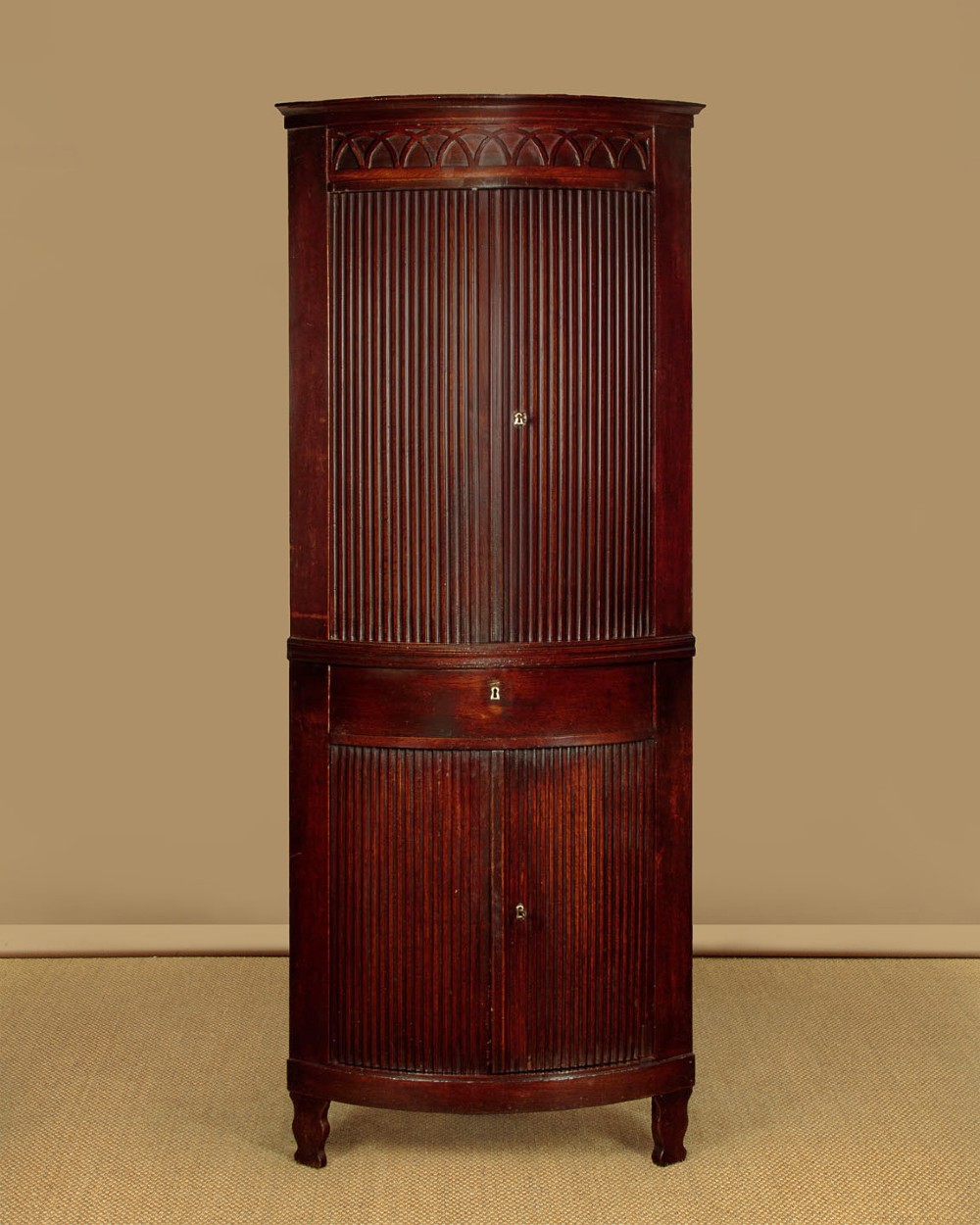 A tall early 19th-century dark mahogany double height corner cupboard featuring reeded front doors, a central drawer, and Gothic arcading at the cornice.