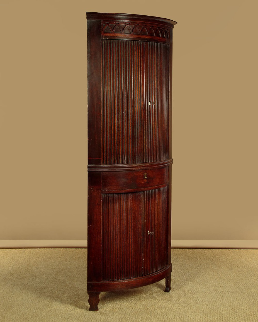 A tall early 19th-century dark mahogany double height corner cupboard featuring reeded front doors, a central drawer, and Gothic arcading at the cornice. View II