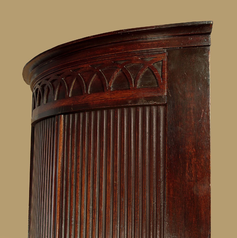 A tall early 19th-century dark mahogany double height corner cupboard featuring reeded front doors, a central drawer, and Gothic arcading at the cornice. View V