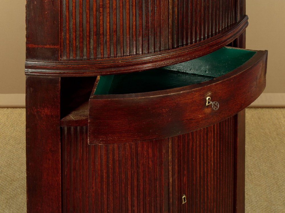 A tall early 19th-century dark mahogany double height corner cupboard featuring reeded front doors, a central drawer, and Gothic arcading at the cornice. View VIII