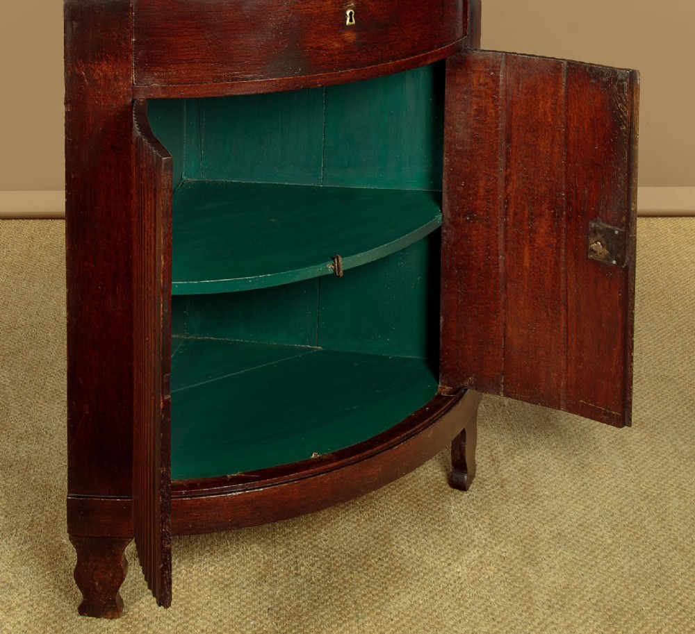 A tall early 19th-century dark mahogany double height corner cupboard featuring reeded front doors, a central drawer, and Gothic arcading at the cornice. View IX