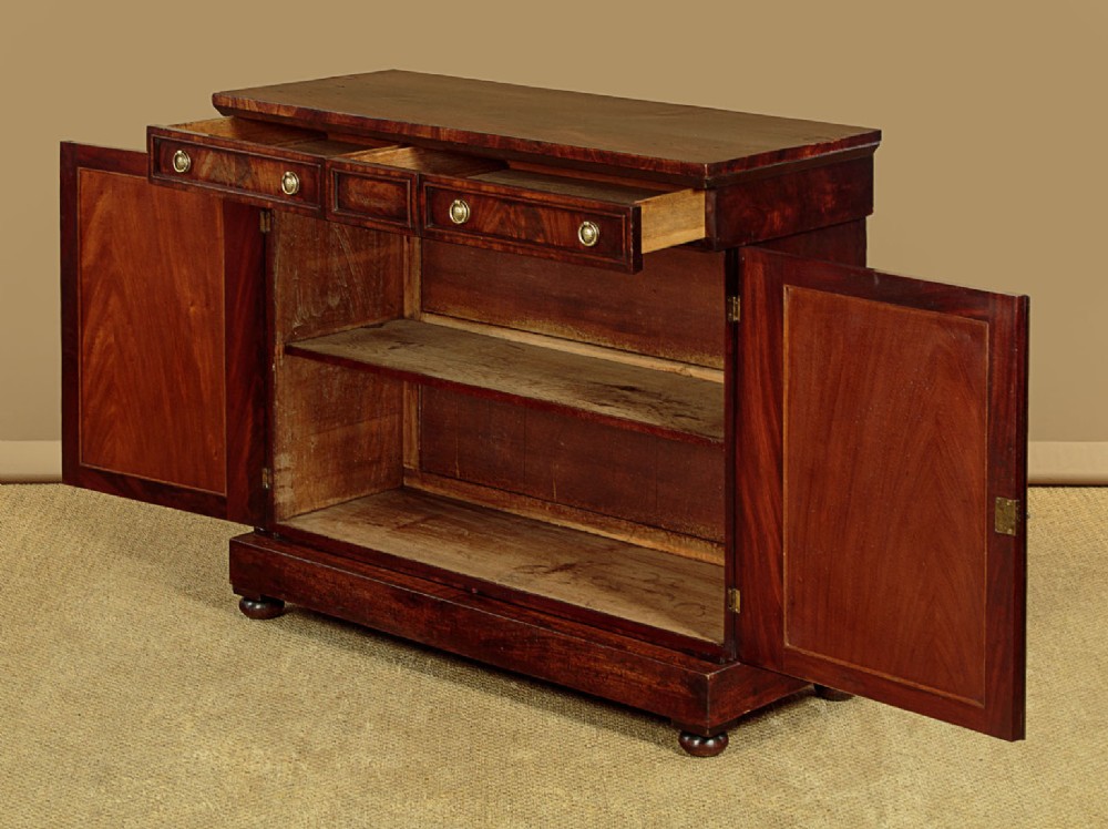 A Victorian flame mahogany chiffonier cabinet featuring frieze drawers with brass ring pulls and twin panelled cupboard doors on a plinth base. View IV