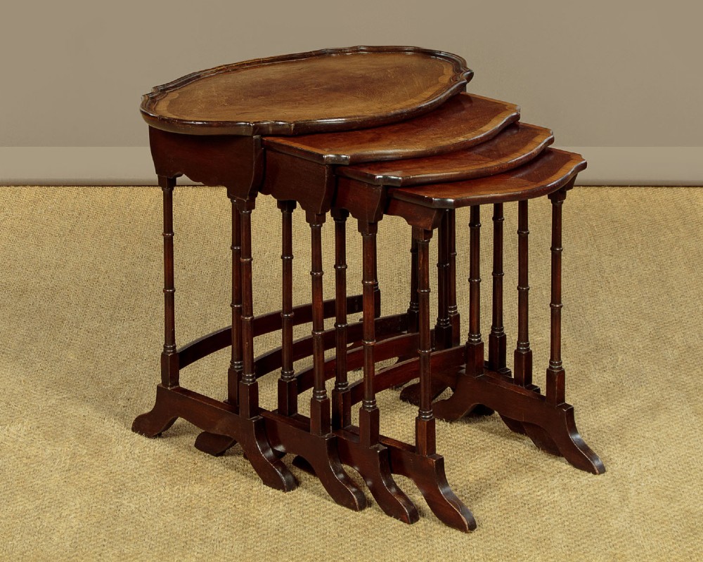 A set of four graduated dark mahogany quartetto nesting tables featuring turned spindle legs and shaped tops.
