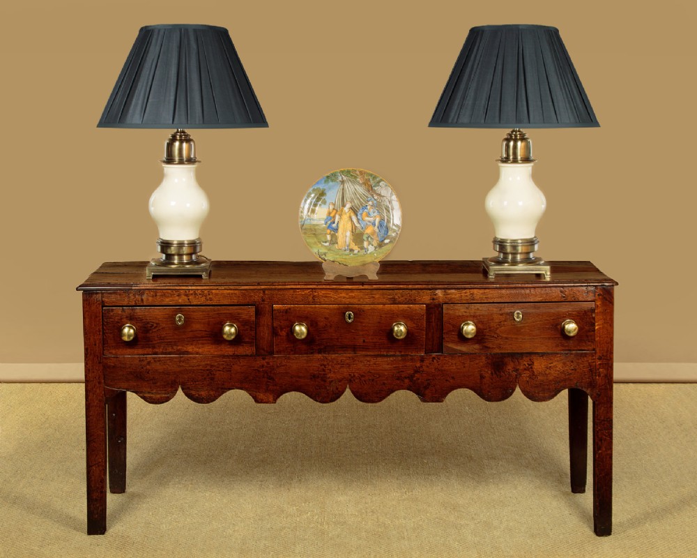 An 18th-century oak dresser base featuring three drawers with brass knobs, a scalloped lower apron, and four straight legs. View II