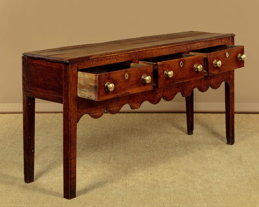 An 18th-century oak dresser base featuring three drawers with brass knobs, a scalloped lower apron, and four straight legs. View III
