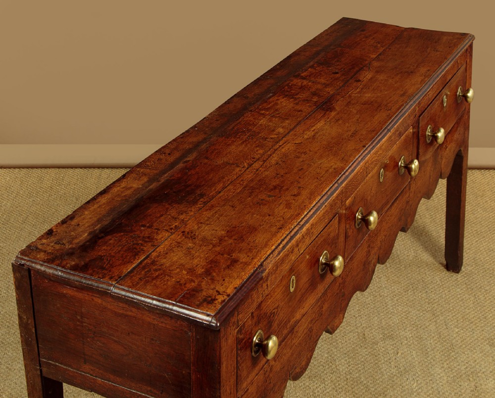 An 18th-century oak dresser base featuring three drawers with brass knobs, a scalloped lower apron, and four straight legs. View IV