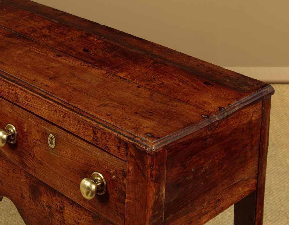 An 18th-century oak dresser base featuring three drawers with brass knobs, a scalloped lower apron, and four straight legs. View V