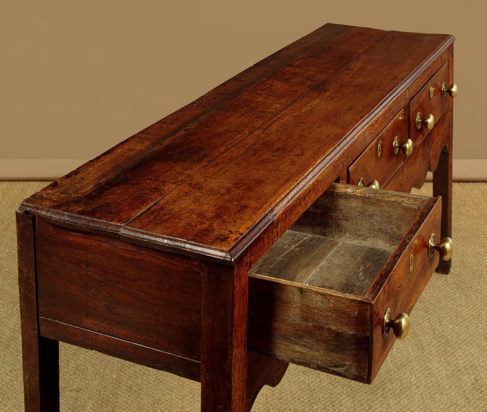 An 18th-century oak dresser base featuring three drawers with brass knobs, a scalloped lower apron, and four straight legs. View VI