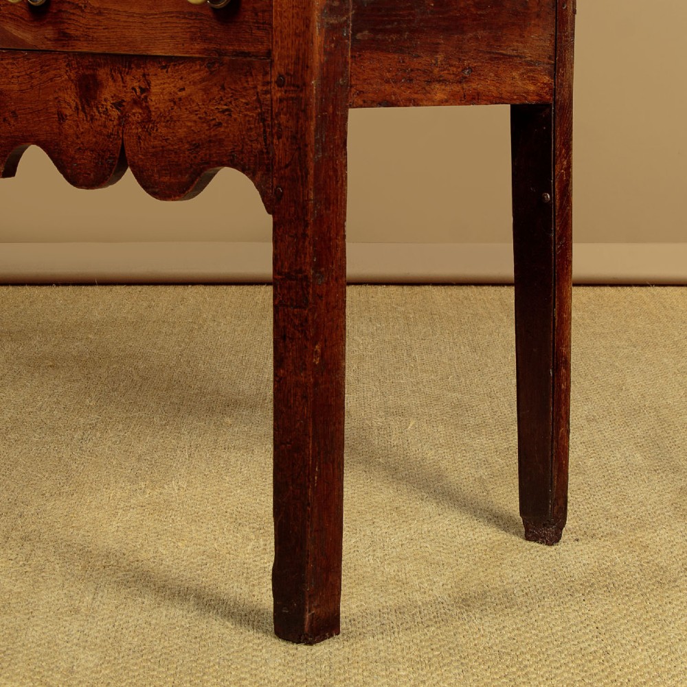 An 18th-century oak dresser base featuring three drawers with brass knobs, a scalloped lower apron, and four straight legs. View IX