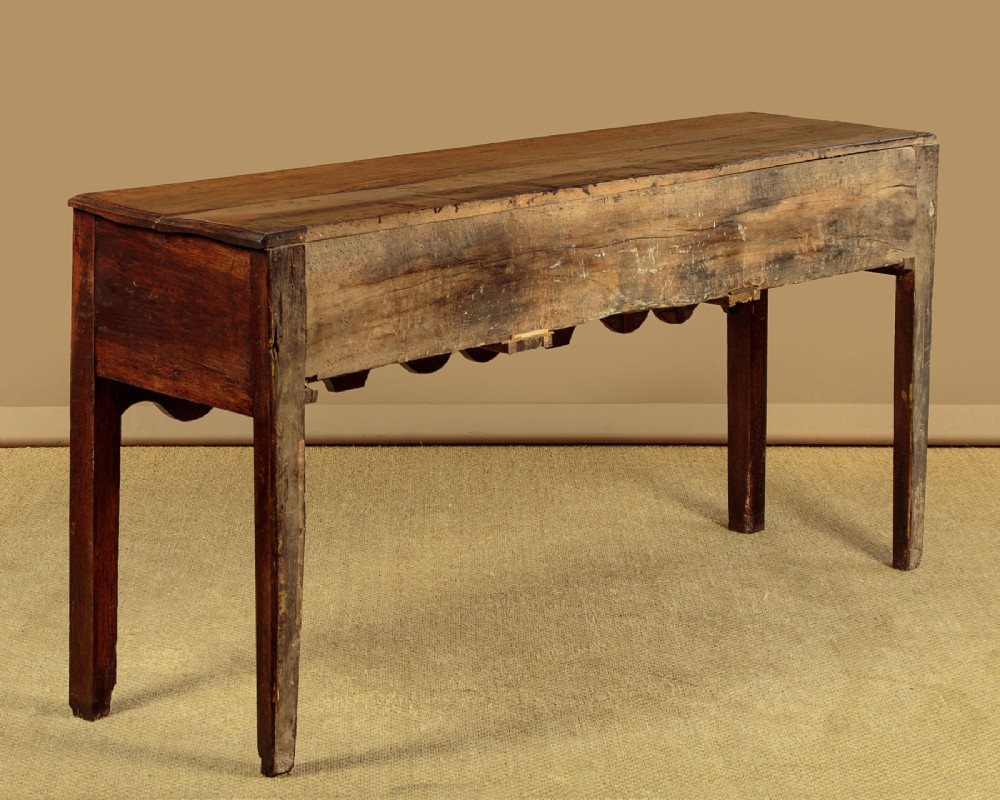 An 18th-century oak dresser base featuring three drawers with brass knobs, a scalloped lower apron, and four straight legs. View X