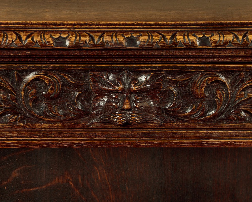 A low late Victorian dark oak open bookcase with detailed foliate relief carvings, brass ring fittings on side pilasters, and adjustable shelves. View VIII