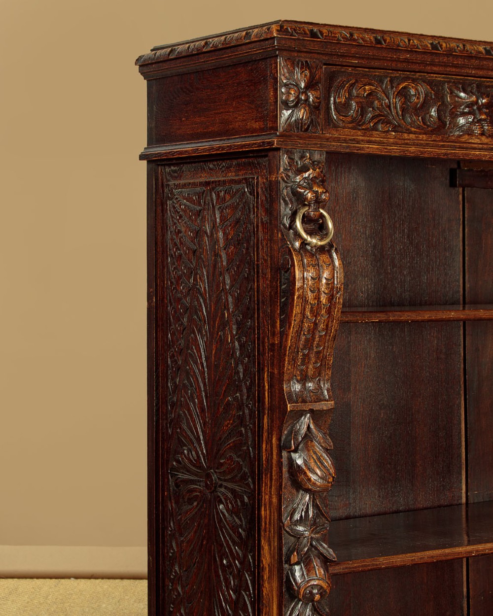 A low late Victorian dark oak open bookcase with detailed foliate relief carvings, brass ring fittings on side pilasters, and adjustable shelves. View IX