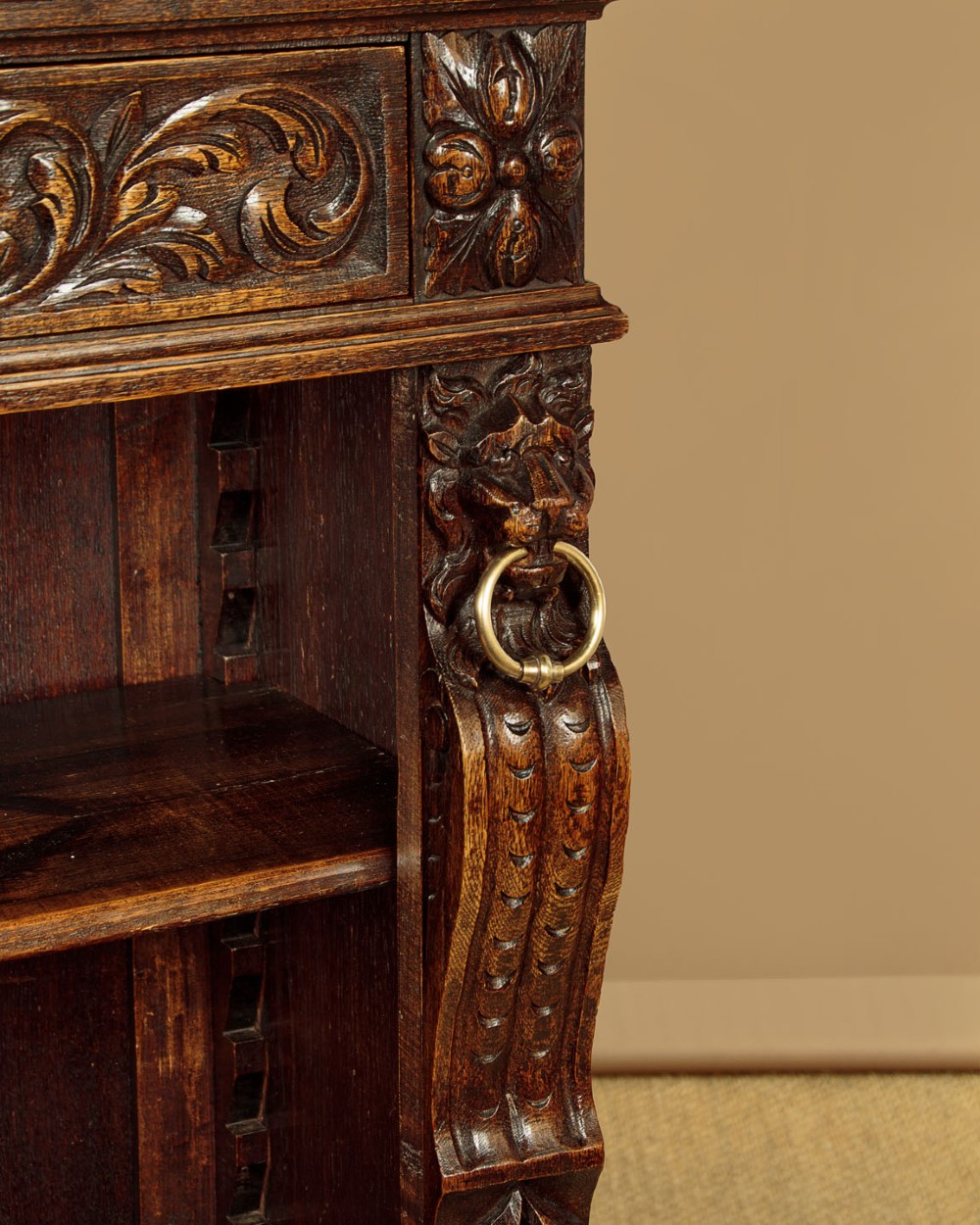 A low late Victorian dark oak open bookcase with detailed foliate relief carvings, brass ring fittings on side pilasters, and adjustable shelves. View XI
