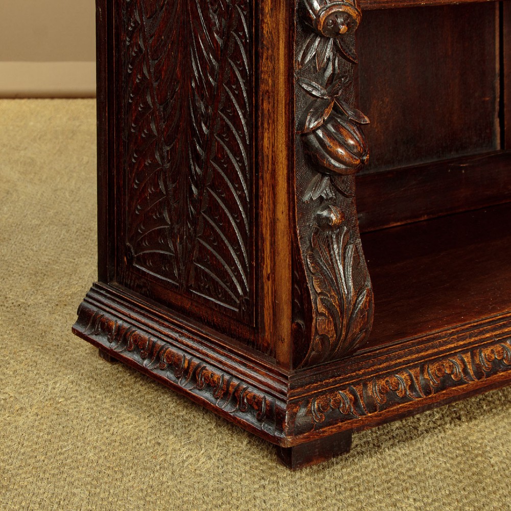 A low late Victorian dark oak open bookcase with detailed foliate relief carvings, brass ring fittings on side pilasters, and adjustable shelves. View XII