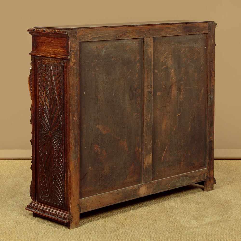 A low late Victorian dark oak open bookcase with detailed foliate relief carvings, brass ring fittings on side pilasters, and adjustable shelves. View XIII