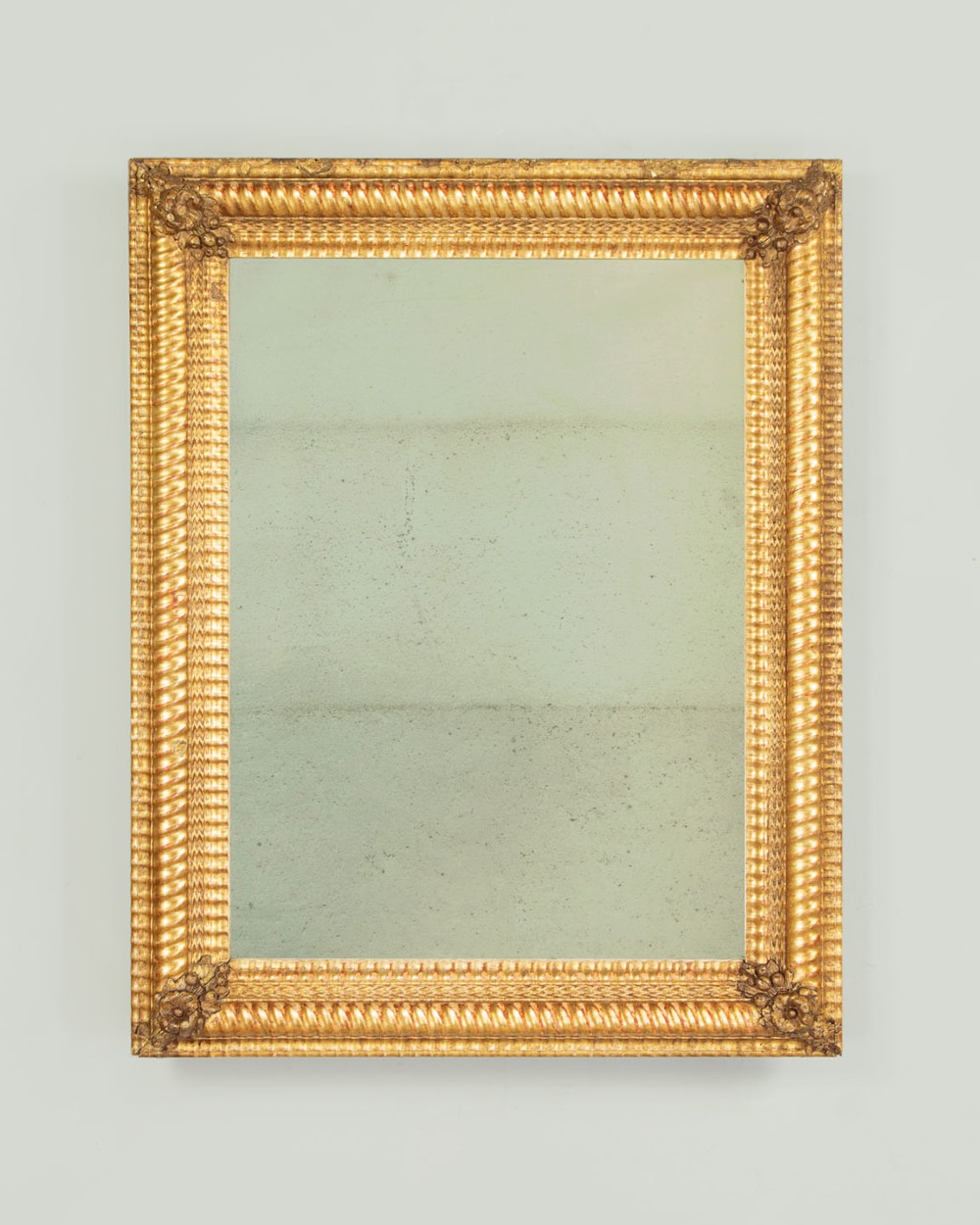 A small rectangular 19th-century French giltwood mirror with textured frame moulding and carved corner rosettes.