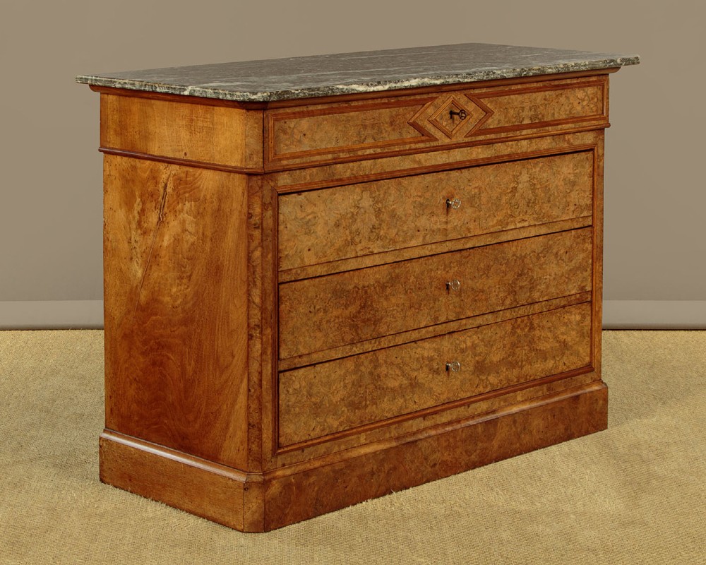 A nineteenth-century burr walnut commode featuring a grey marble top surface, a upper drawer with a central diamond inlay, three long lower drawers, and a plinth base. View III