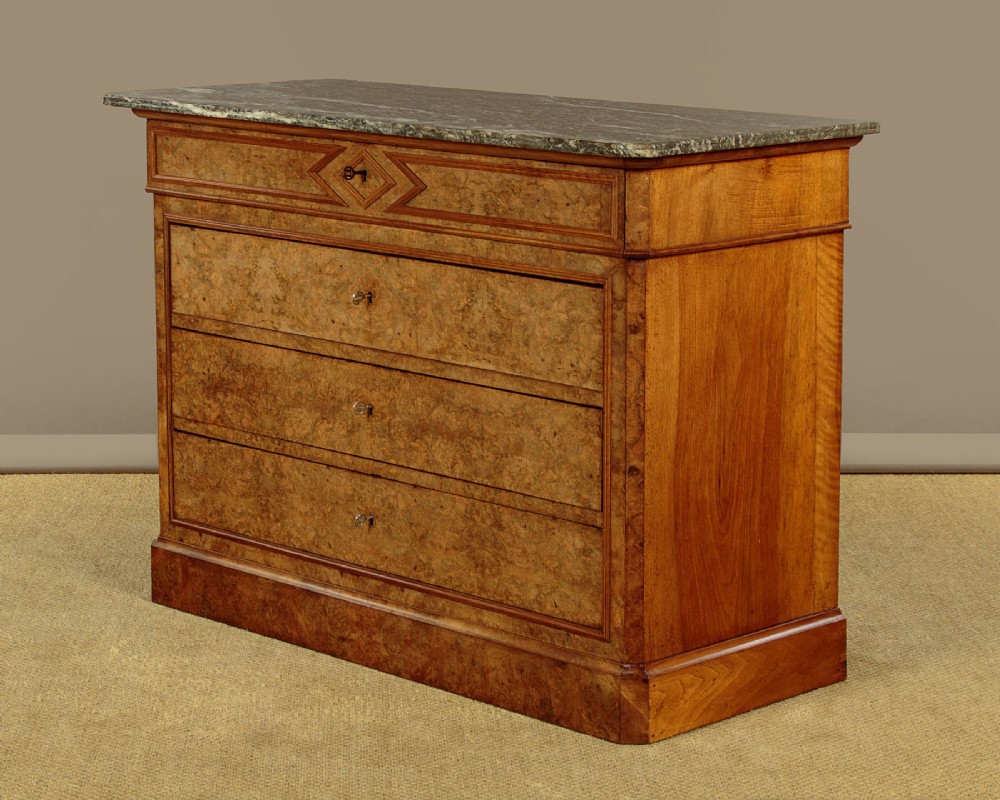 A nineteenth-century burr walnut commode featuring a grey marble top surface, a upper drawer with a central diamond inlay, three long lower drawers, and a plinth base. View IV