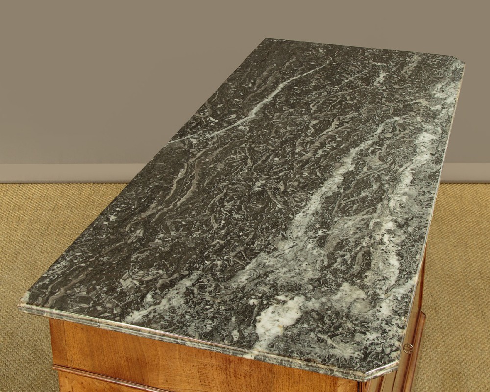 A nineteenth-century burr walnut commode featuring a grey marble top surface, a upper drawer with a central diamond inlay, three long lower drawers, and a plinth base. View VI