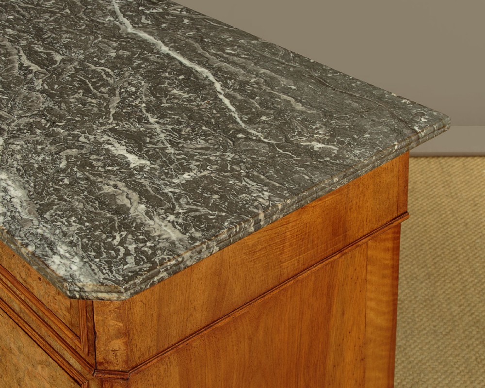 A nineteenth-century burr walnut commode featuring a grey marble top surface, a upper drawer with a central diamond inlay, three long lower drawers, and a plinth base. View VII