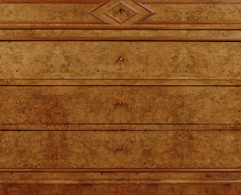 A nineteenth-century burr walnut commode featuring a grey marble top surface, a upper drawer with a central diamond inlay, three long lower drawers, and a plinth base. View IX