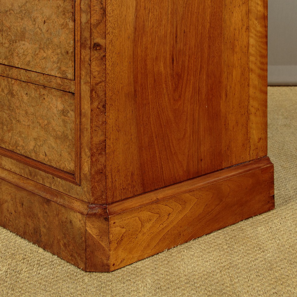 A nineteenth-century burr walnut commode featuring a grey marble top surface, a upper drawer with a central diamond inlay, three long lower drawers, and a plinth base. View XII
