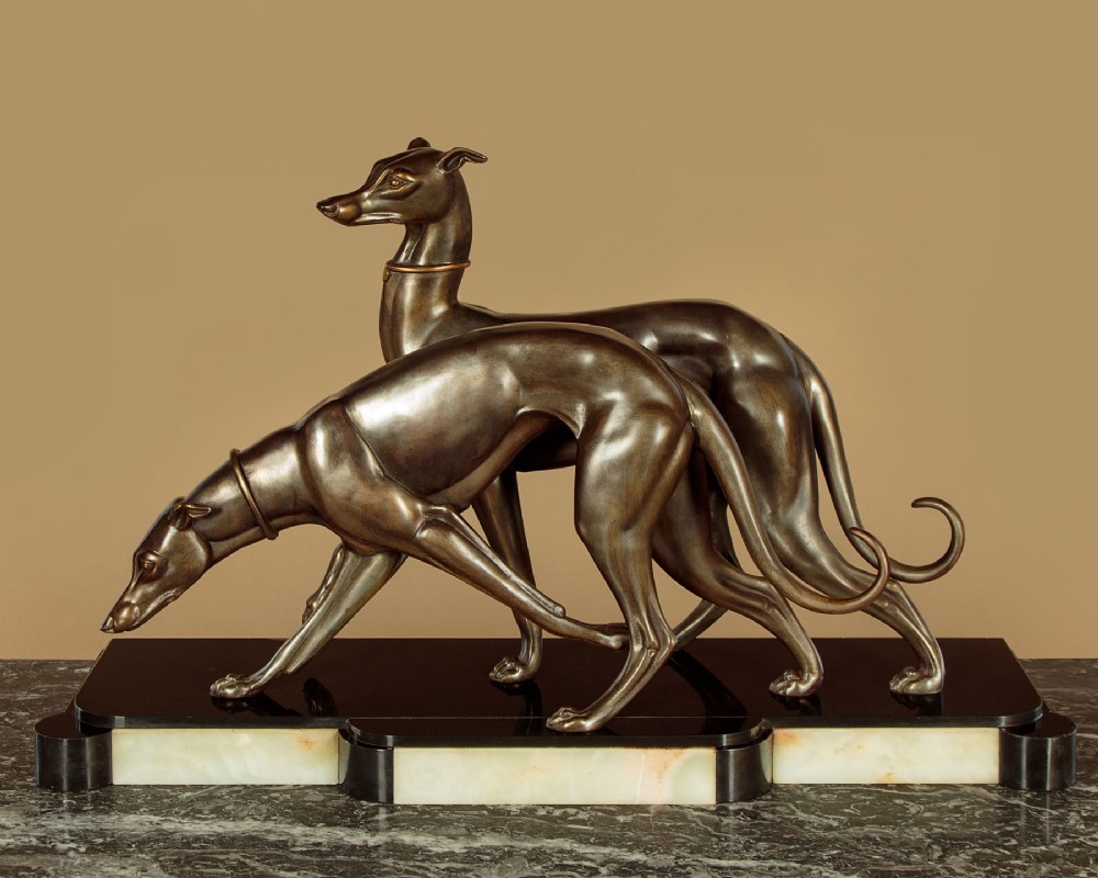 An Art Deco dark bronze sculpture featuring two sleek greyhounds poised on a stepped black marble and cream onyx base.