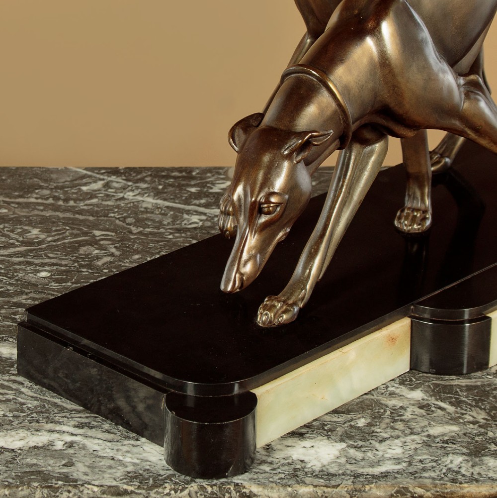 An Art Deco dark bronze sculpture featuring two sleek greyhounds poised on a stepped black marble and cream onyx base. View X