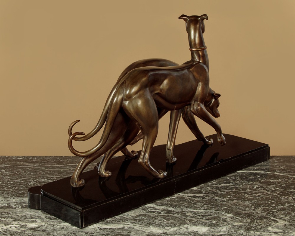 An Art Deco dark bronze sculpture featuring two sleek greyhounds poised on a stepped black marble and cream onyx base. View XII