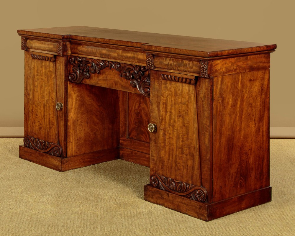 An early Victorian flame mahogany pedestal sideboard featuring carved scrollwork across the central apron and pedestal cupboards set on plinth bases. View III