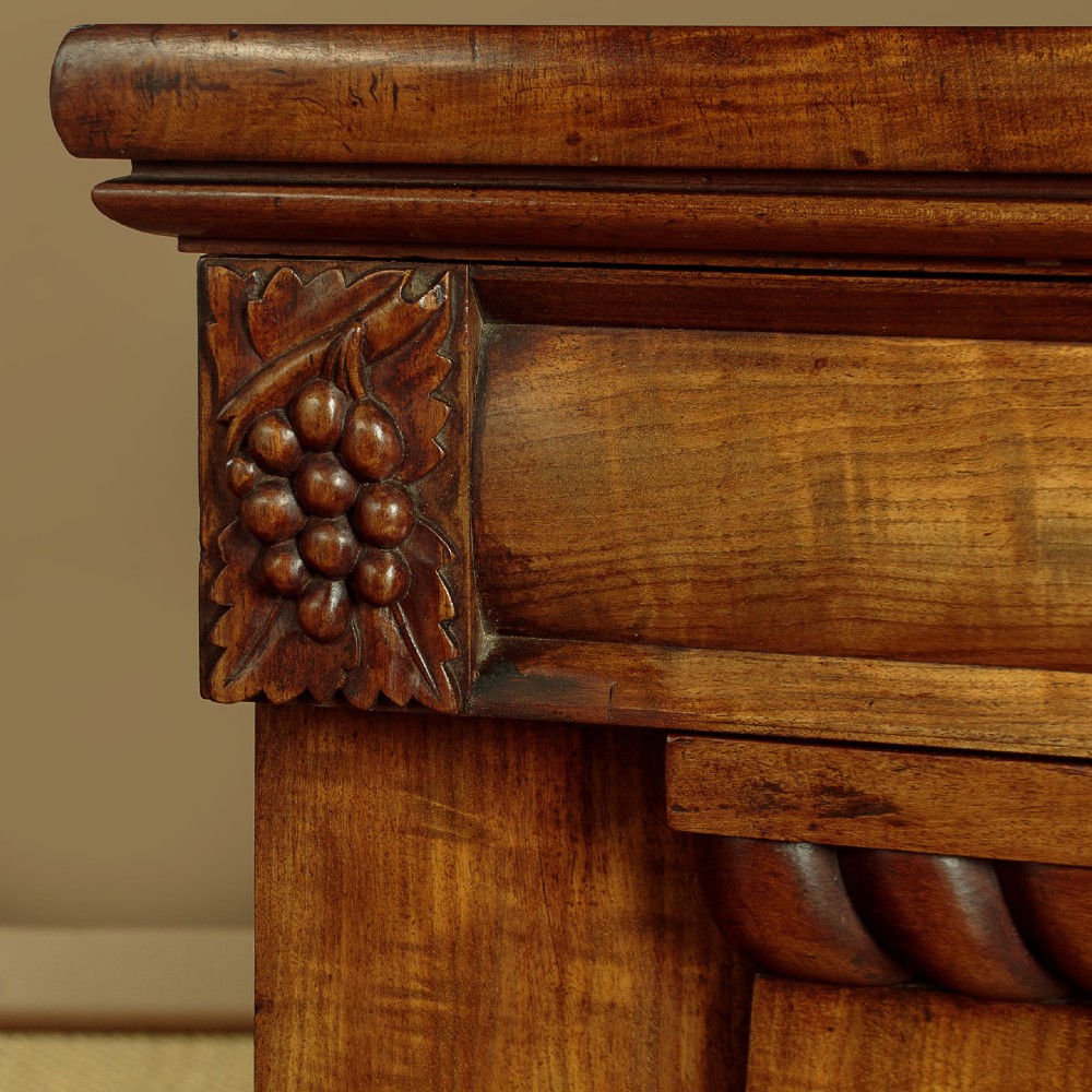 An early Victorian flame mahogany pedestal sideboard featuring carved scrollwork across the central apron and pedestal cupboards set on plinth bases. View VIII