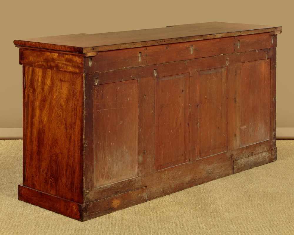 An early Victorian flame mahogany pedestal sideboard featuring carved scrollwork across the central apron and pedestal cupboards set on plinth bases. View XIV
