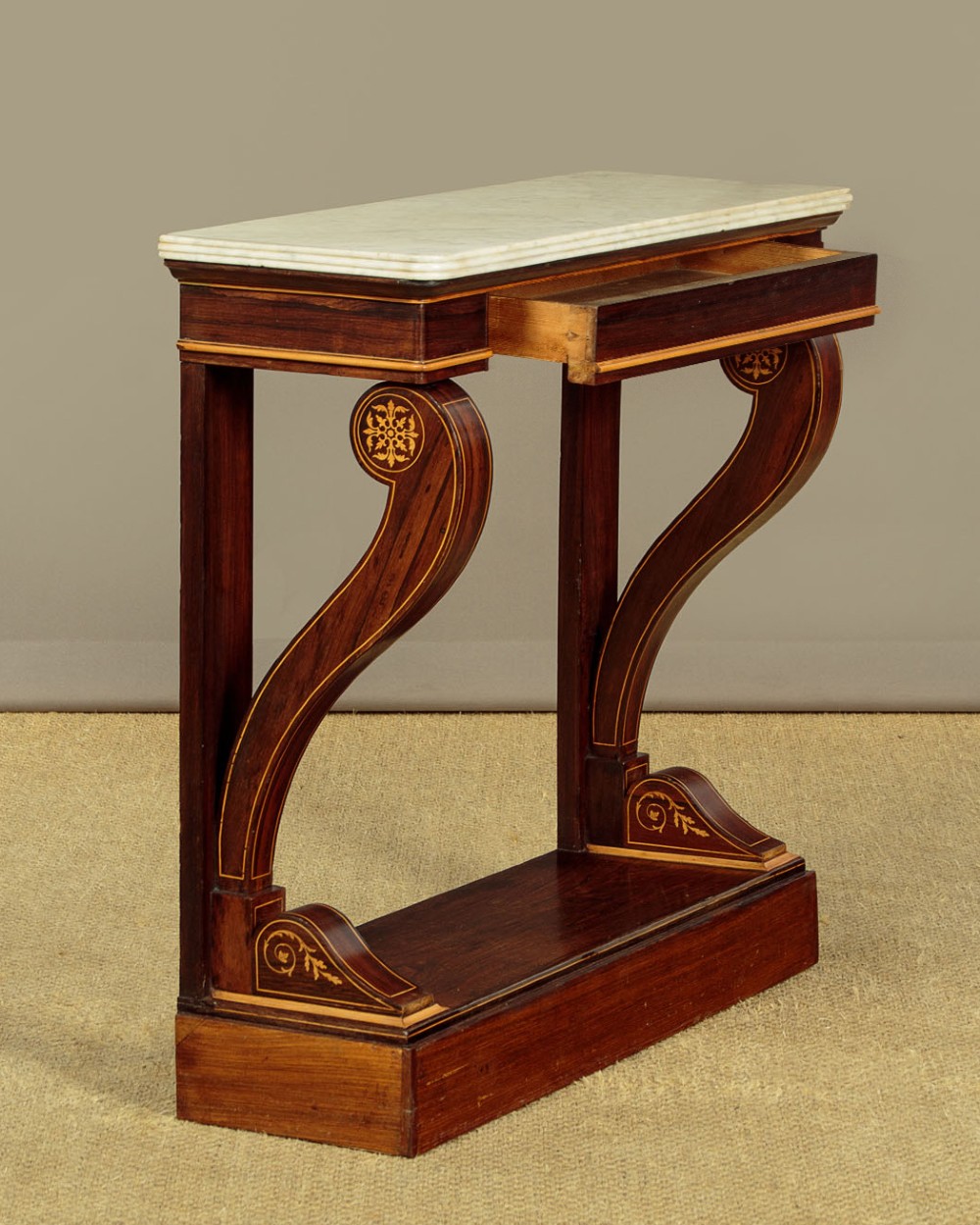 A small late Victorian mahogany console table featuring a white marble top, decorative marquetry on curved scroll legs, a single frieze drawer, and a solid plinth base.