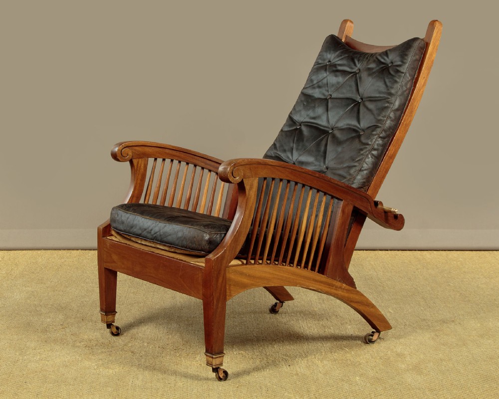 An Arts and Crafts adjustable reclining armchair in polished hardwood with slatted side panels and dark brown tufted leather cushions.