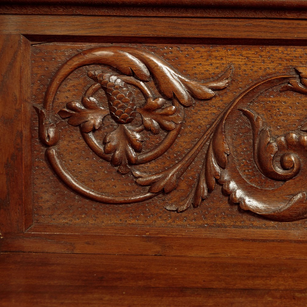 A carved dark oak hall bench featuring a scroll decorated backrest, carved relief panels with an urn motif, turned fluted front legs, and shaped side armrests. View VI