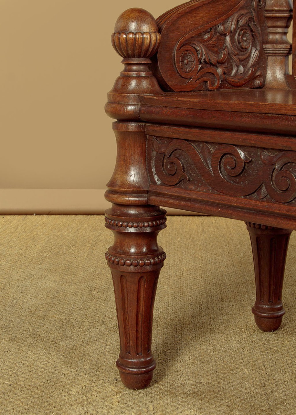A carved dark oak hall bench featuring a scroll decorated backrest, carved relief panels with an urn motif, turned fluted front legs, and shaped side armrests. View XIII